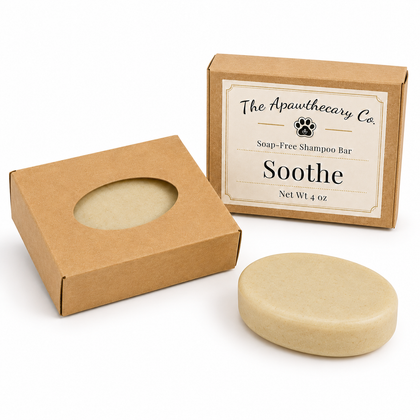 A soap-free shampoo bar in a round beige bar form, shown next to its kraft paper packaging boxes. The box features a circular cutout displaying the bar and a second box with a front label reading 'The Apawthecary Co.