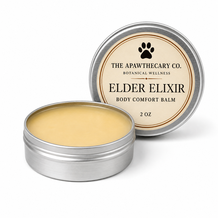 An open round silver tin of Elder Elixir Body Comfort Balm by The Apawthecary Co., showing the pale yellow balm inside, with the matching lid standing behind it on a white background.