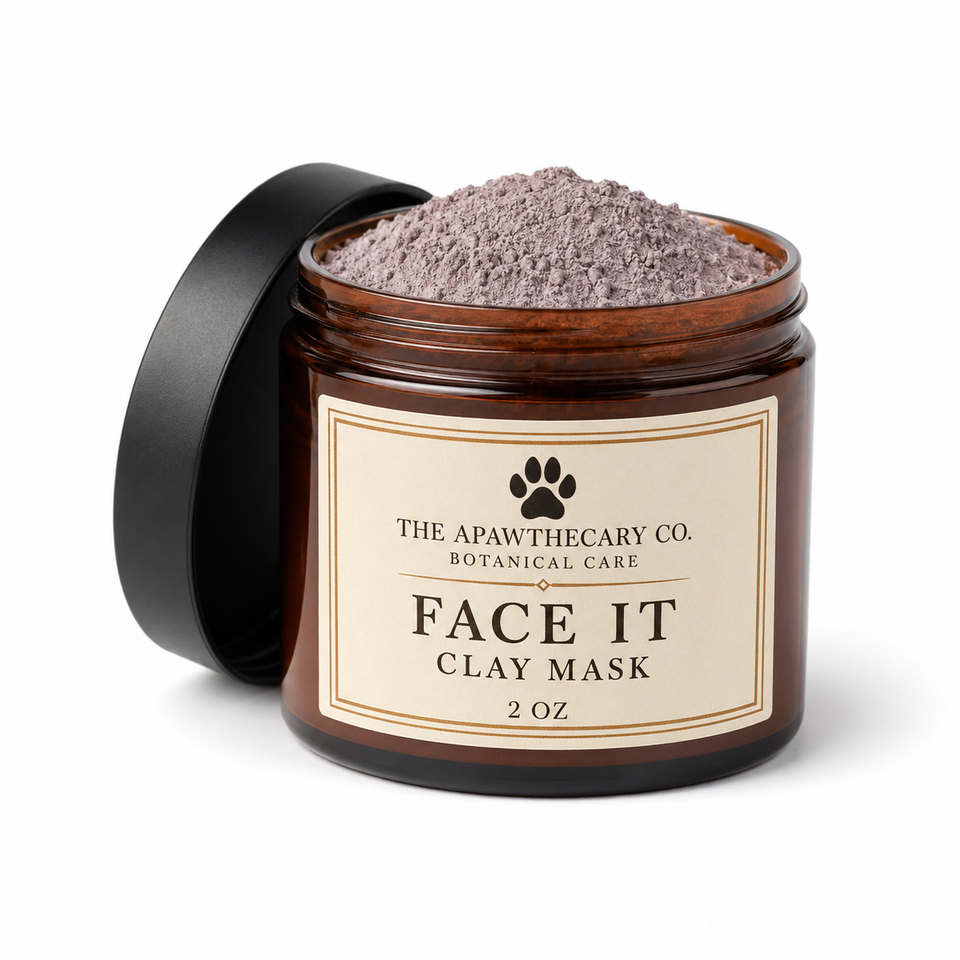 An amber glass jar of The Apawthecary Co. Face It Clay Mask with its black lid leaning against it on a white background.