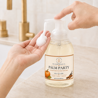 A bottle of The Apothecary Co. Palm Party Turmeric Spiced Foaming Hand Soap is shown on a bathroom counter with a faucet in the background.