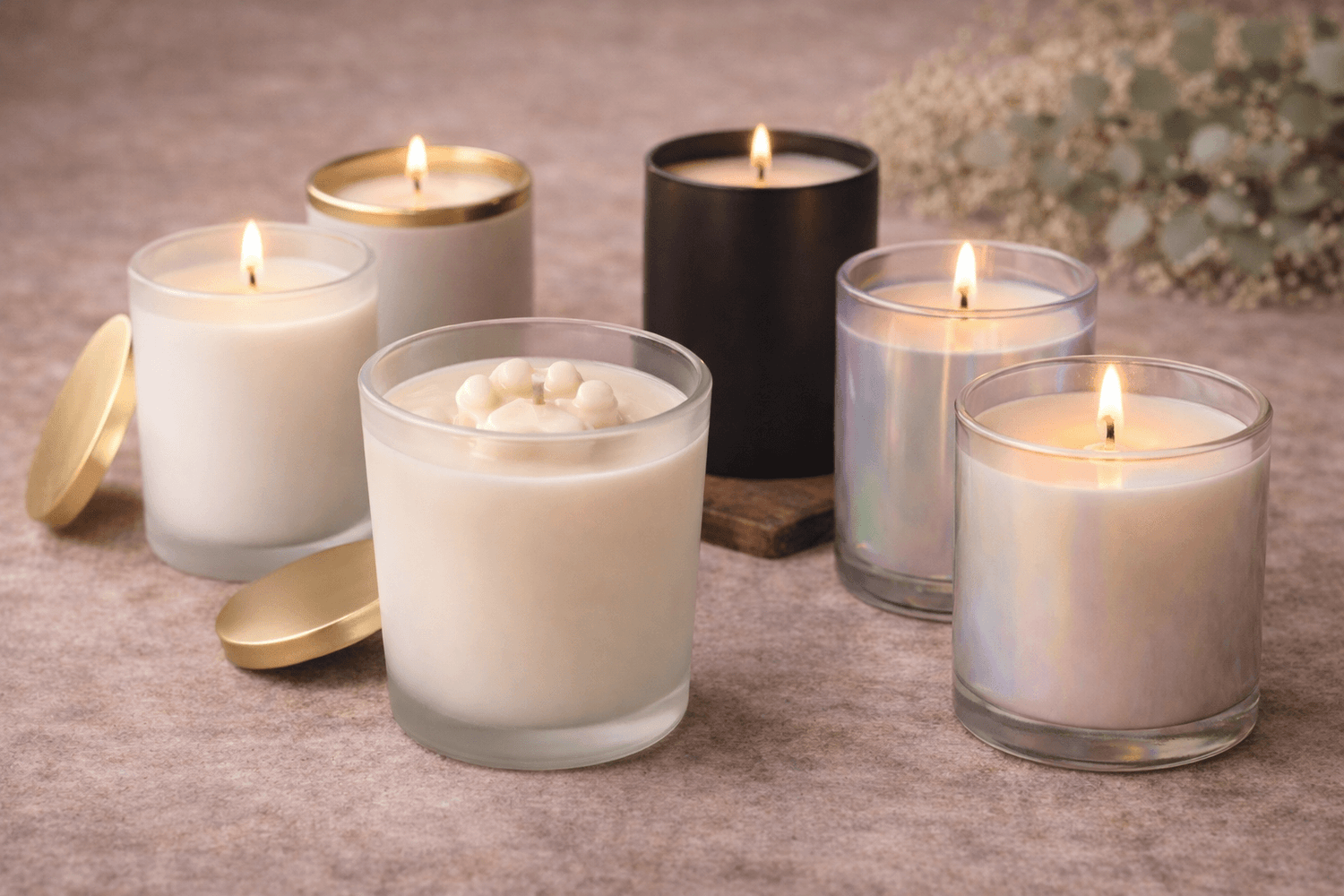 Set of candles in various containers on a textured surface with a blurred floral background