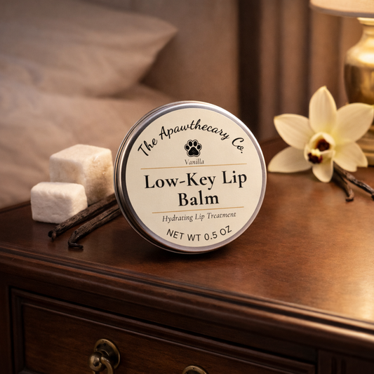 Low-Key Lip Balm container on a wooden surface with vanilla beans and an orchid in the background.