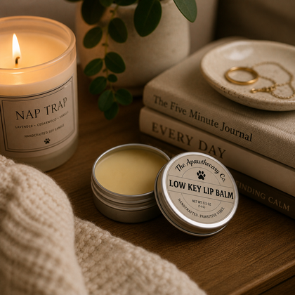 Low-Key Lip Balm - Vanilla & Marshmallow tin placed on a wooden table next to a candle and books.