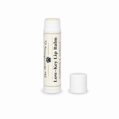 A tube of Low-Key Lip Balm by The Apothecary Co. in Pumpkin & Vanilla scent, shown with its cap off next to it on a clean white background.