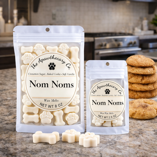 Two packages of 'Nom Noms' wax melts from The Apawthecary Co. on a kitchen counter with cookies.