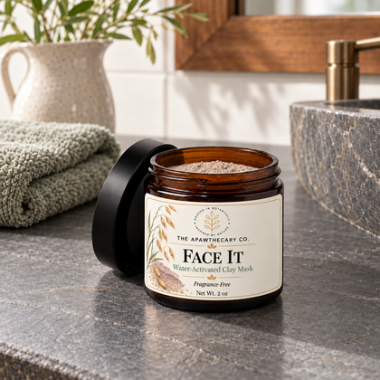 Open Face It clay mask jar beside folded towels and a soap dispenser at a bathroom sink.