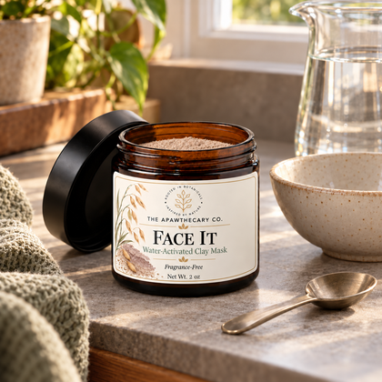 Open Face It clay mask jar beside a mixing bowl, spoon and water pitcher on a bathroom counter.