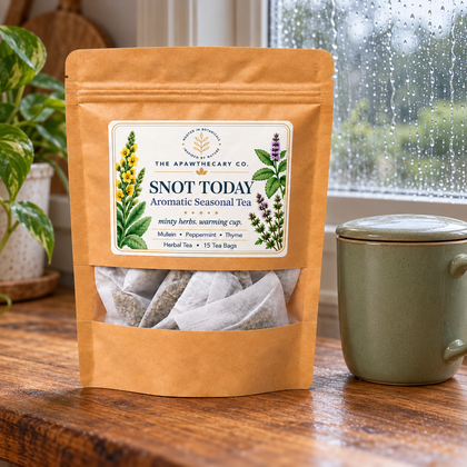Snot Today herbal tea pouch beside a green lidded mug on a table by a rain-speckled window.