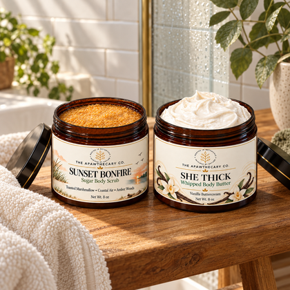 Open jars of Sunset Bonfire sugar body scrub and She Thick whipped body butter on a wooden bench beside a shower.