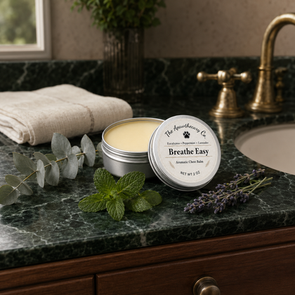Open tin of Breathe Easy aromatic balm beside folded towels and green botanicals on a dark countertop.