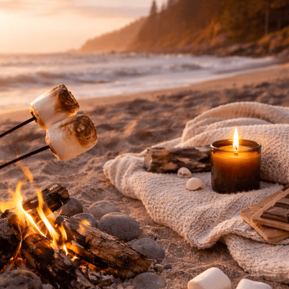 Marshmallows roasting over a campfire on a beach with a candle and blanket.
