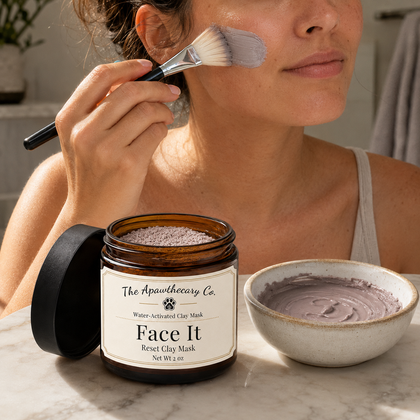 Woman applying a mixed Face It clay mask with a brush beside the open jar and mixing bowl.