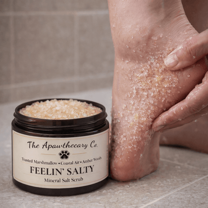 Person applying 'Feelin' Salty' mineral salt scrub to their foot with a jar of the product next to them.