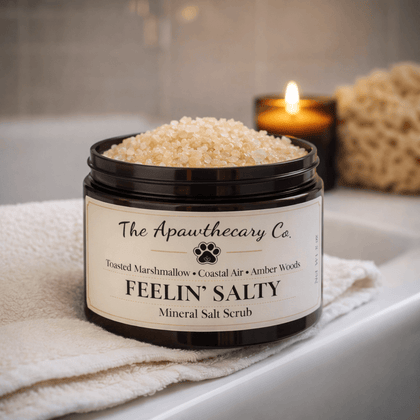 Jar of 'Feelin' Salty' mineral salt scrub from The Apothecary Co. on a bathtub ledge with a candle and sponge in the background.
