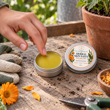 Palm-sized Herbal Skin Salve 2 oz tin on a garden workbench beside an adult hand.