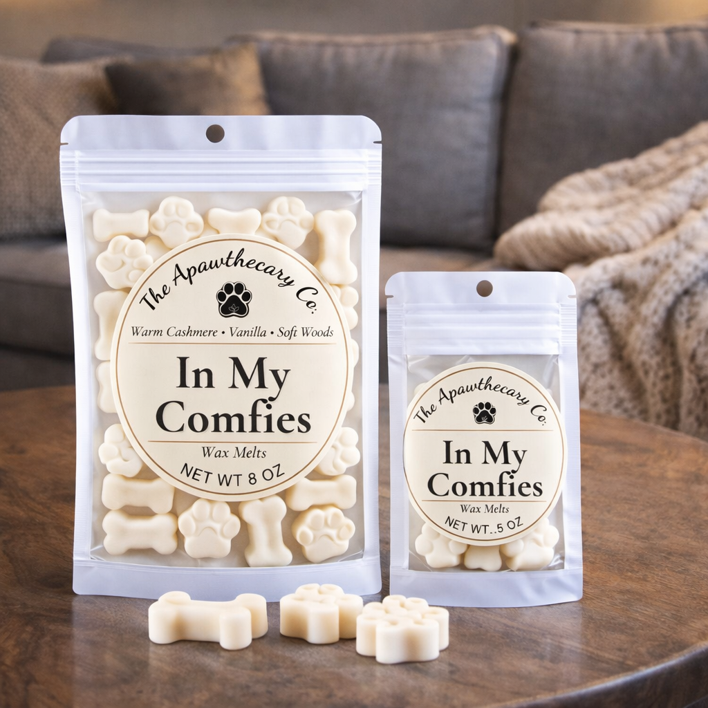 Two packages of 'In My Comfies' wax melts from The Apawthecary Co on a wooden surface with a blurred couch in the background.