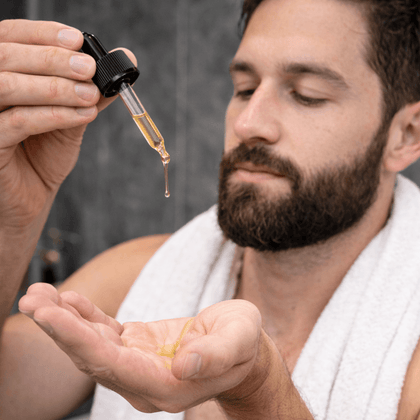 Man applying lightweight beard oil from dropper to hand for grooming and beard care.