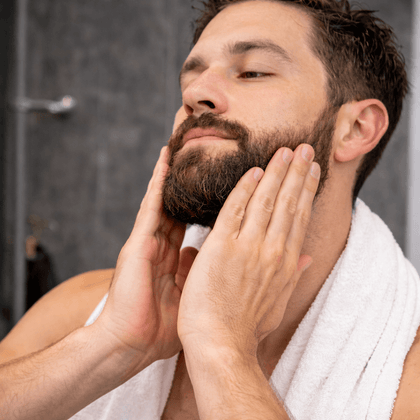 Man with a beard applying cream to his face in a bathroom setting