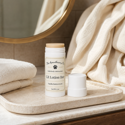 A lit lotion bar in a white container with a beige cap, displayed on a marble tray with folded cream towels and a draped fabric in the background.