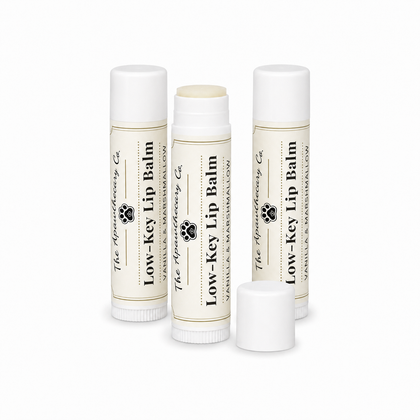 Three Low-Key Lip Balm tubes in vanilla and marshmallow, with one tube open on a white background.