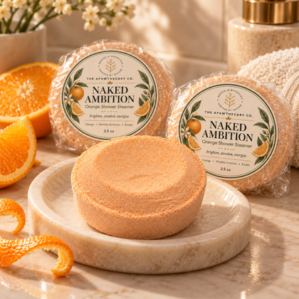 Naked Ambition orange shower steamer on a spa-style vanity with orange and towel