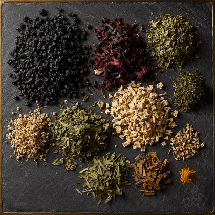 An overhead flat-lay of multiple loose dried herbs, spices, and botanical piles arranged on a dark slate background.