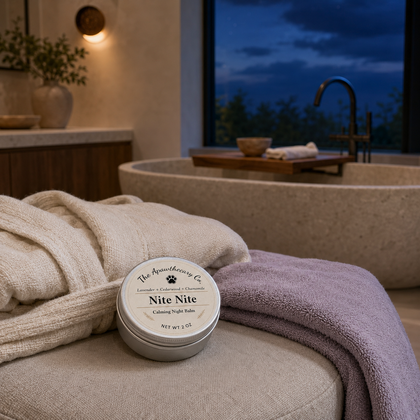 Tin of Nite Nite aromatic balm on a cushioned bench beside folded towels and a stone tub.