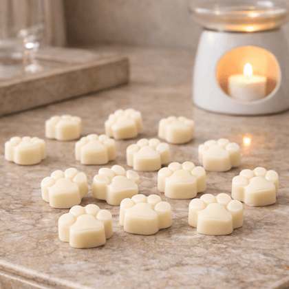 Soy & coconut wax melts shaped like paw prints on a countertop next to a candle, offering a flame-free scent experience.