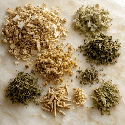 Various loose dried herbal ingredients arranged in small piles on a light marble surface, including tan bark pieces, pale yellow flower heads, and green leaves.