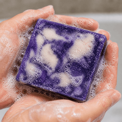 Purple soap bar with white foam in a hand