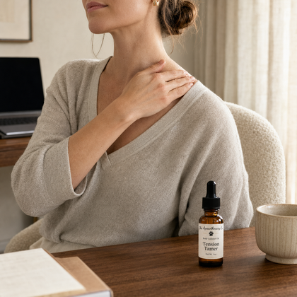 Woman touching her shoulder beside a Tension Tamer oil bottle and a mug on a desk.