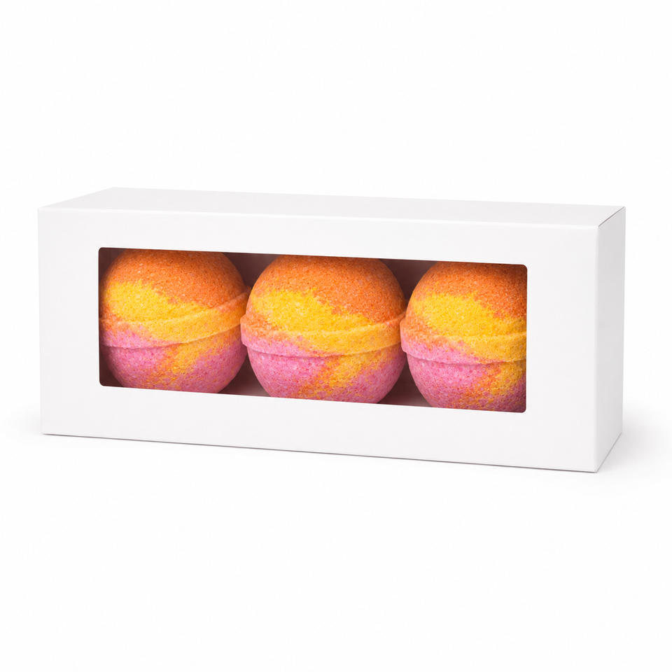 Three round bath bombs with a yellow and pink marbled pattern displayed inside a white rectangular gift box with a clear window, set against a plain white background.